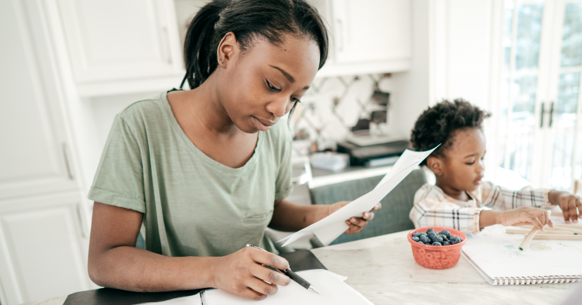 Woman looking at pieces of paper with child in background