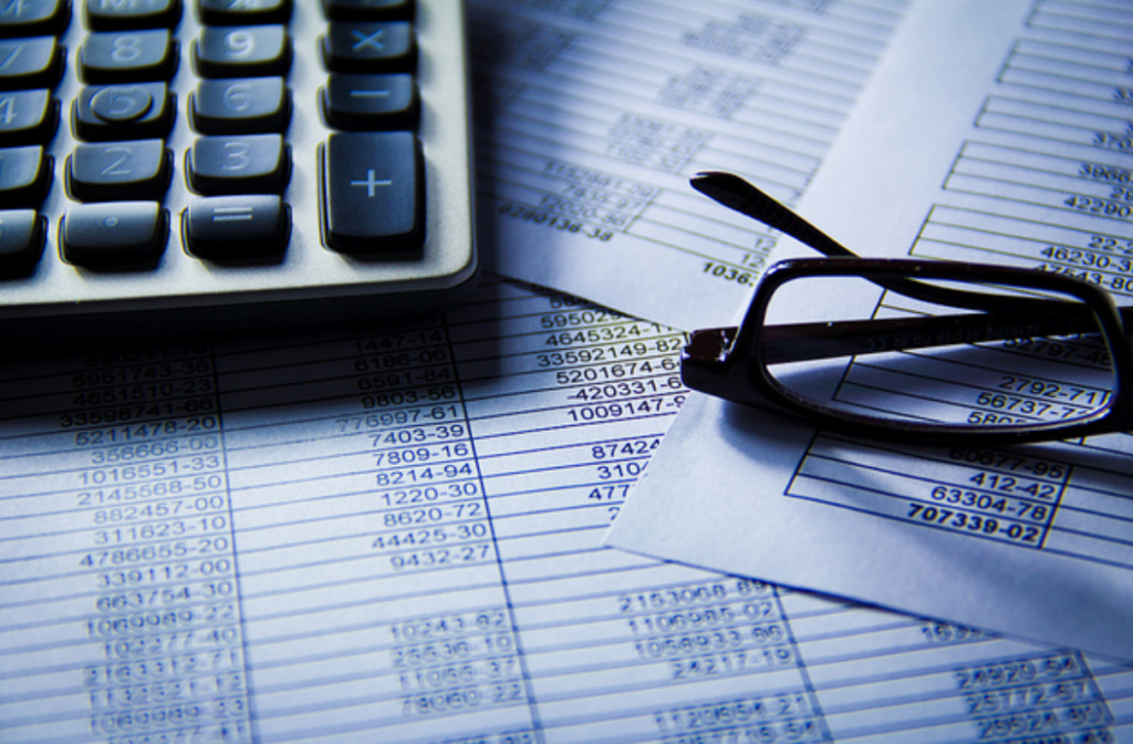numbers in spreadsheet on piece of paper with a pair of glasses and calculator on top