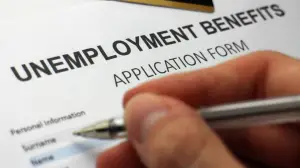 paper that reads "unemployment benefits" with a hand and pen hovering at the top