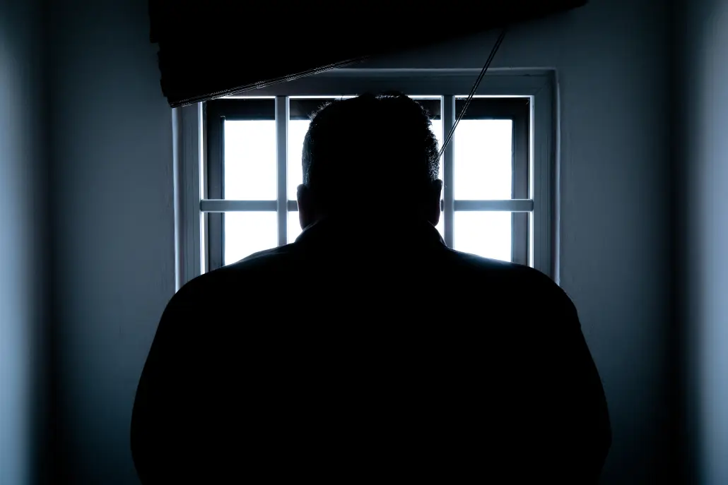 person with back facing the camera looking outside a window with bars