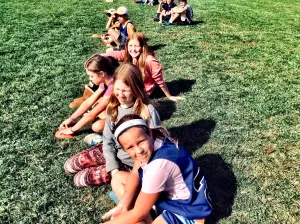 children in a line sitting outside on the grass