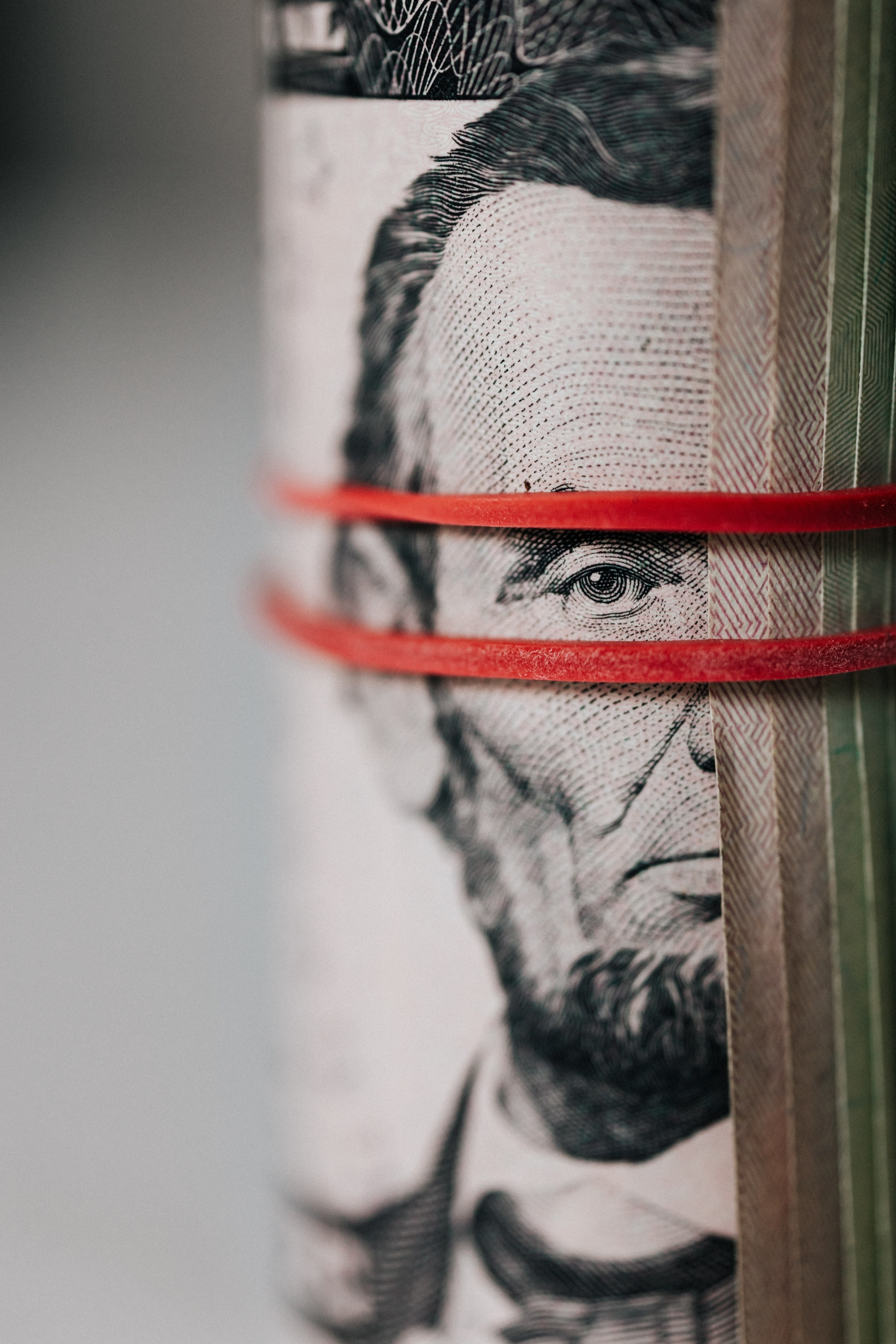 rolled money bill with Lincoln's face centered and a red rubber band wrapped above and below Lincoln's eye