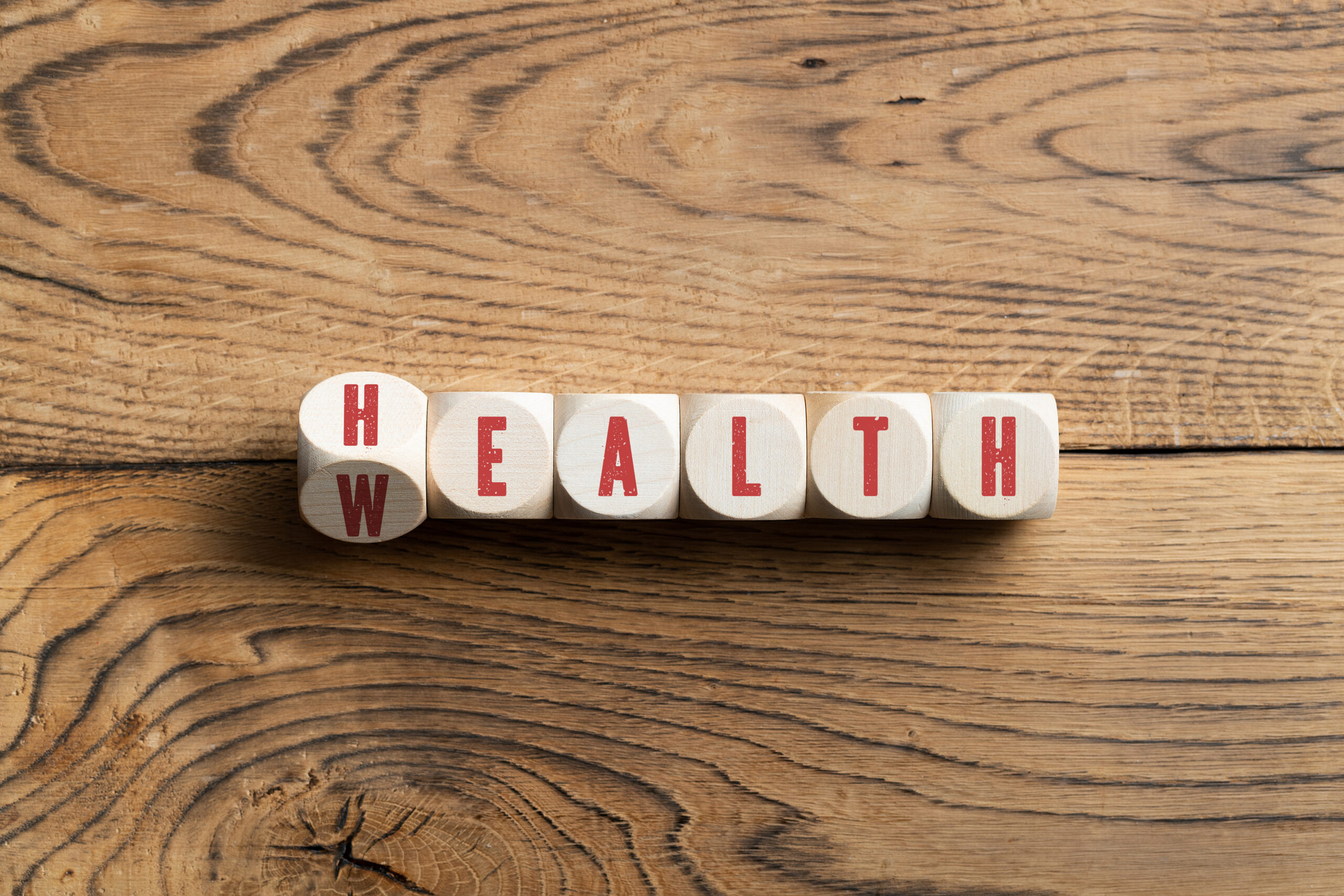 Overhead view on black letters carved on small wooden blocks spelling wealth or health on wood table surface