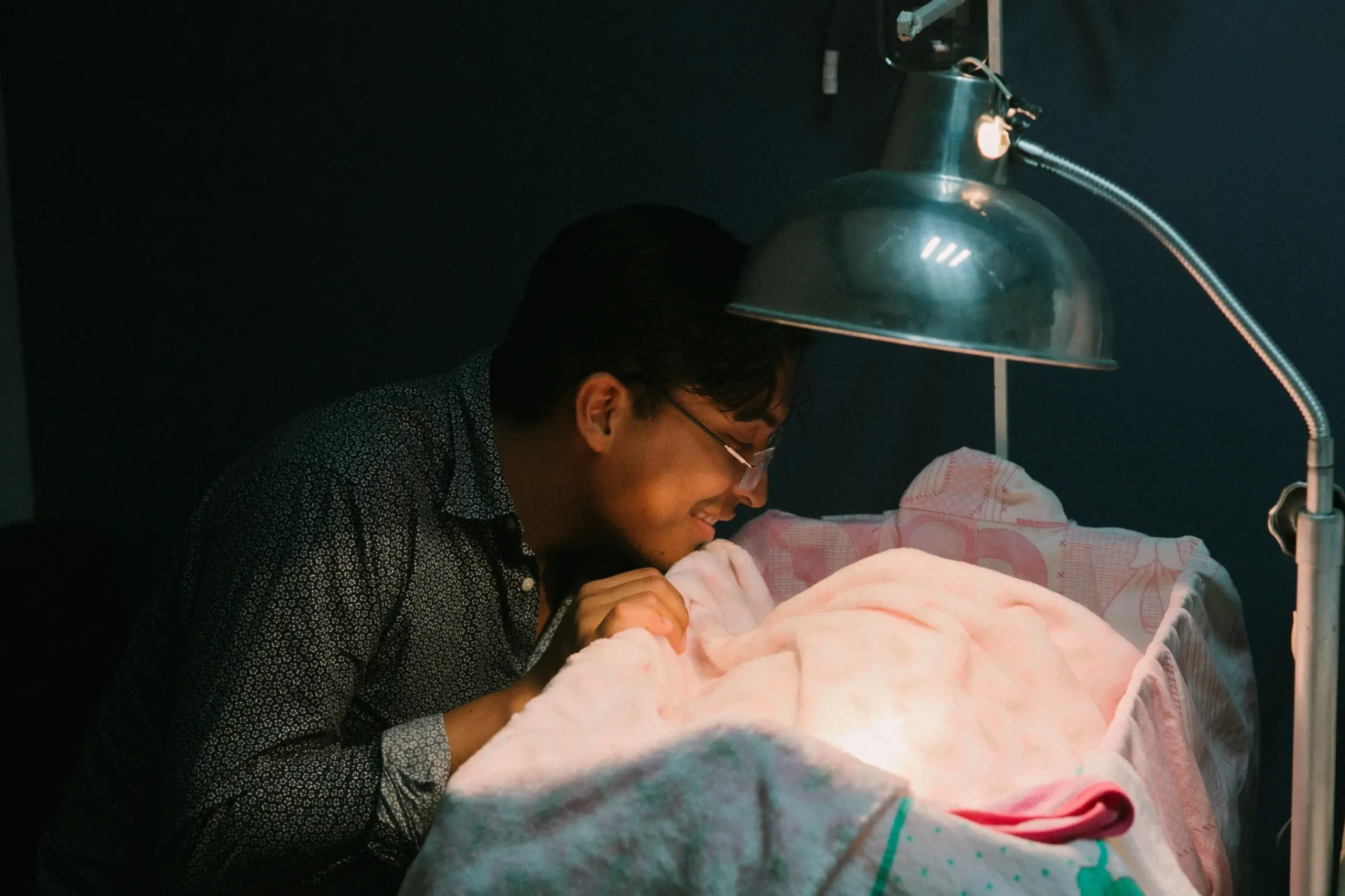 man smiles and looks into a crib with a pink blanket