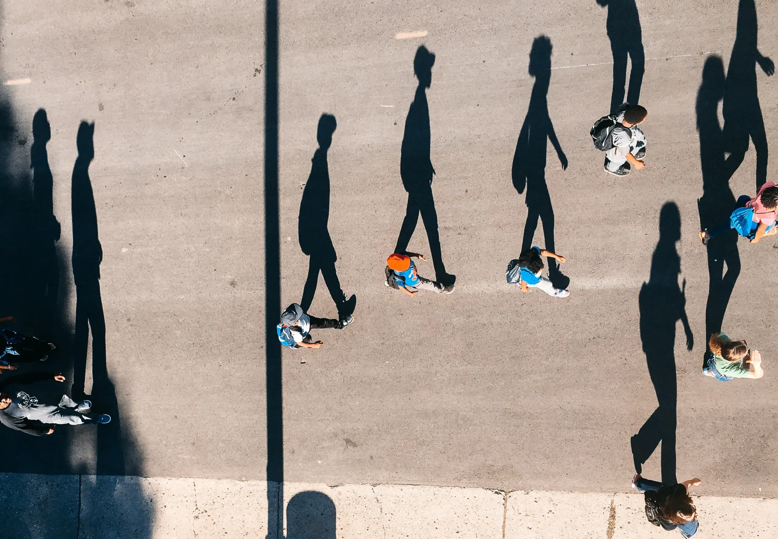 ariel image of men walking with their tall shadows cast beside them